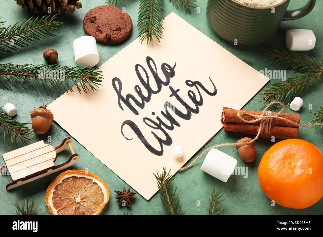 Papier mit Text HALLO WINTER, Leckereien und Weihnachtszweige auf grünem Grunge-Hintergrund Stockfoto