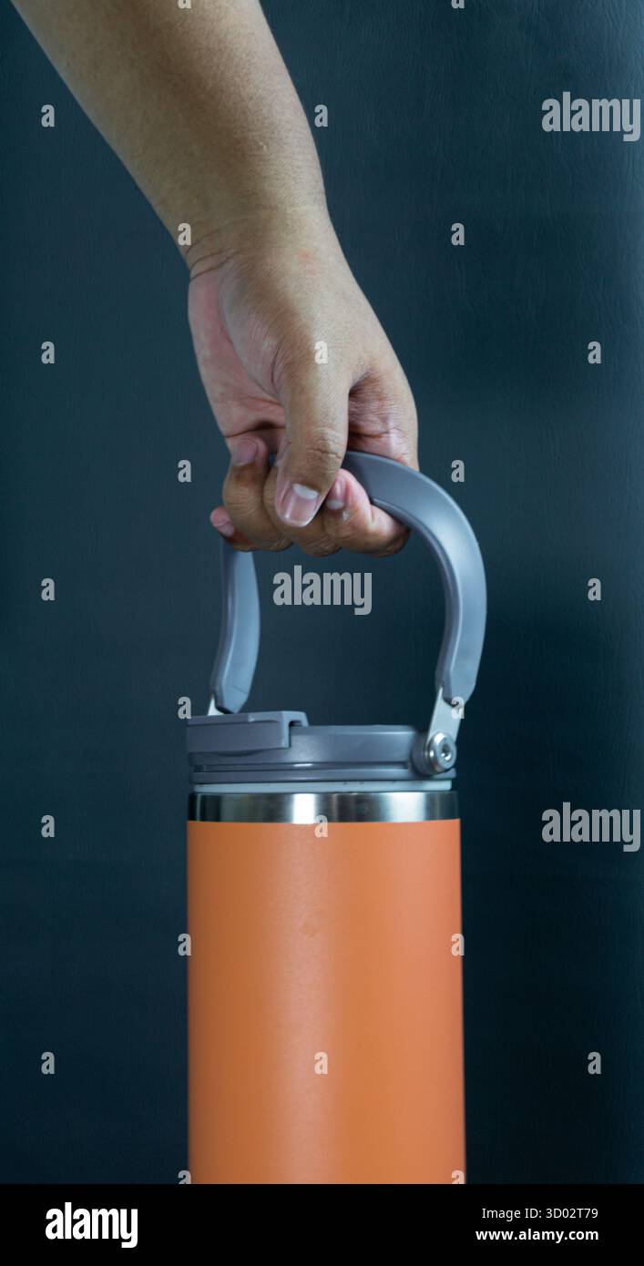 Orangefarbene Trinkflasche am Griff, Portraitrahmen auf schwarzem Hintergrund, sauberes und auffälliges Hydratationskonzept mit modernem Lifestyle-Flair Stockfoto