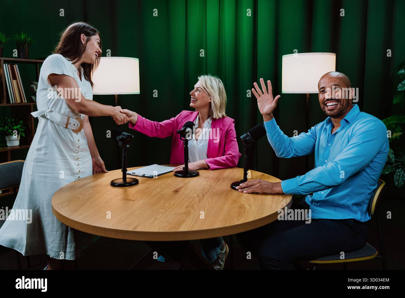 Verschiedene Gastgeber und Gäste in einem Aufnahmestudio, die Hände schütteln und winken, während sie in einer Live-Podcast-Show Themen diskutieren, die Verbindung symbolisieren, welcom Stockfoto