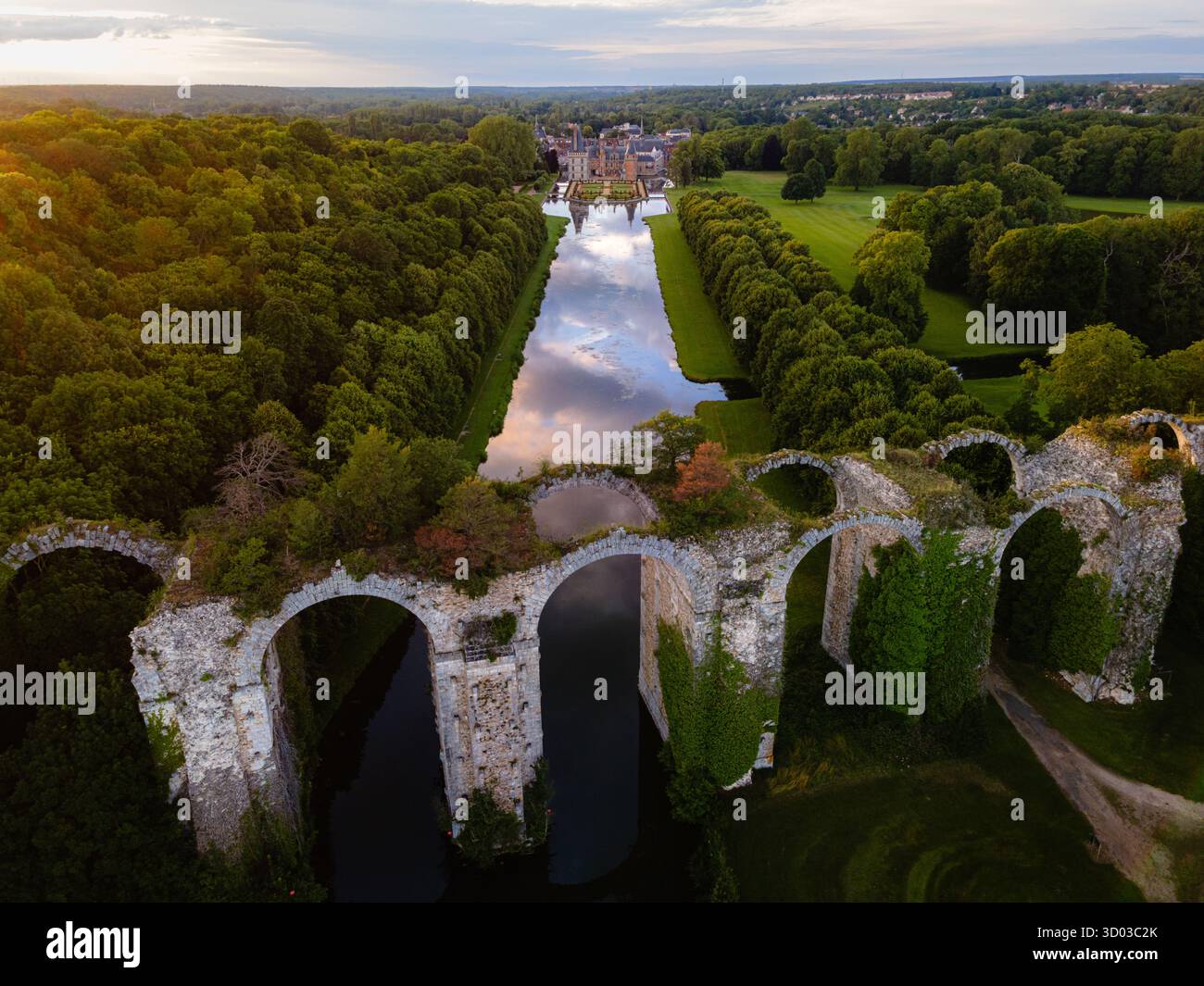 Luftaufnahme eines ruinösen Aquädukts in Maintenon, Frankreich, mit dem château und dem umgebenden parc im Hintergrund, der sich im Kanal unter einem Colorfu spiegelt Stockfoto