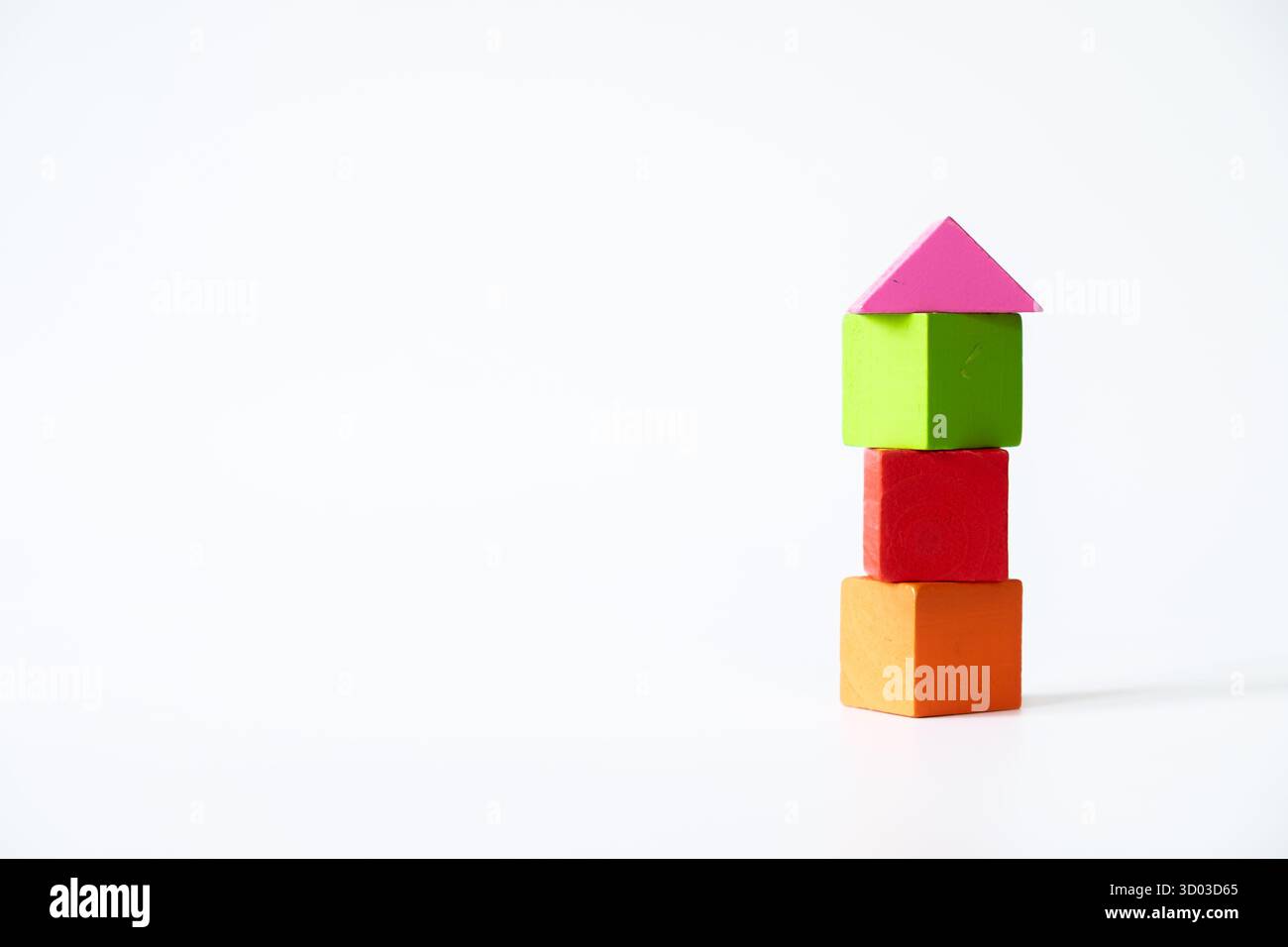 Drei bunte Holzwürfel in Orange, Rot und Grün, die vertikal gestapelt sind und mit einem rosafarbenen Dreiecksblock versehen sind, der einem Haus ähnelt, isoliert auf weißem bac Stockfoto