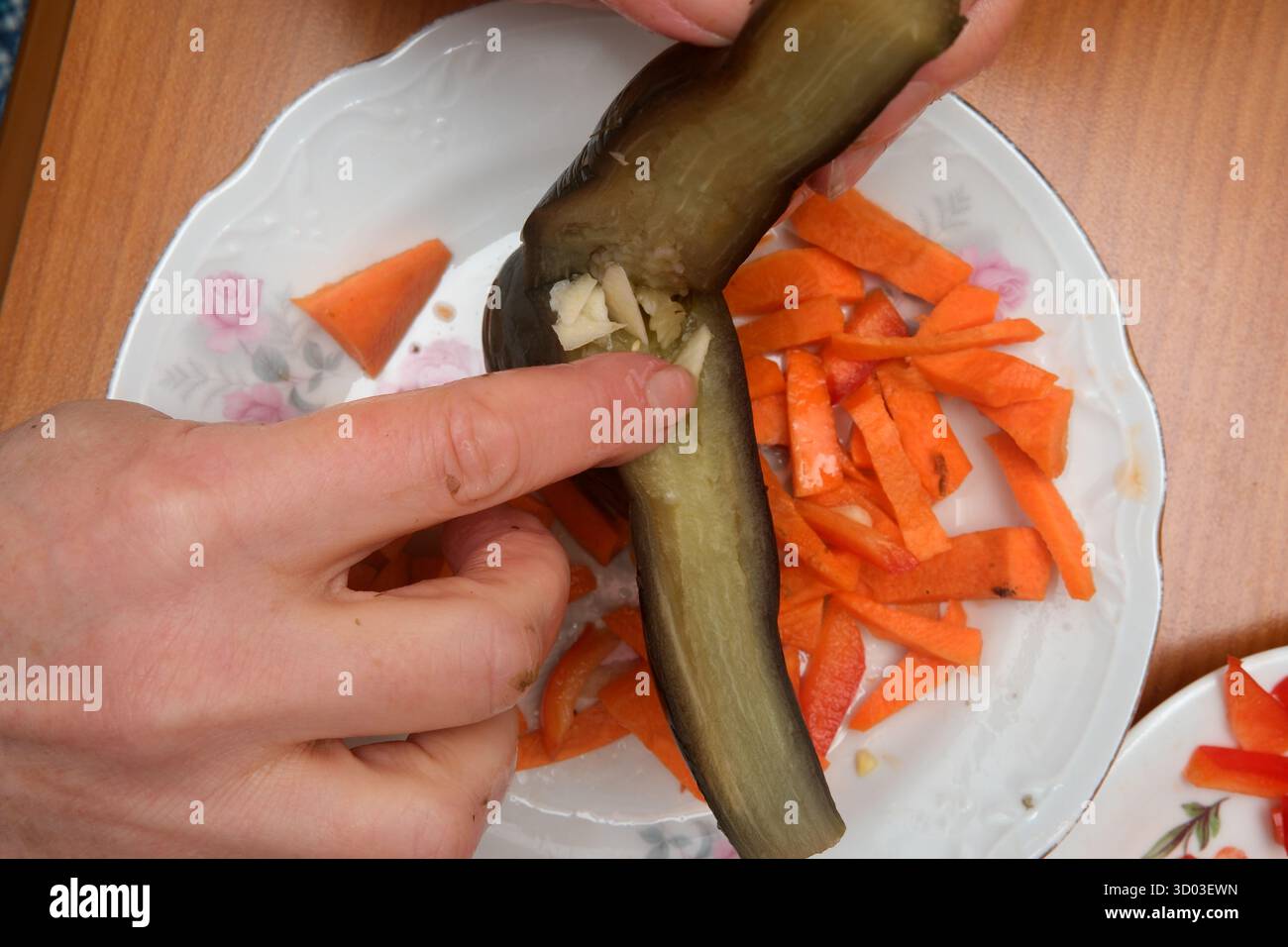 Die Hände bereiten Auberginen gekonnt zum Füllen mit gehacktem Gemüse vor. Stockfoto