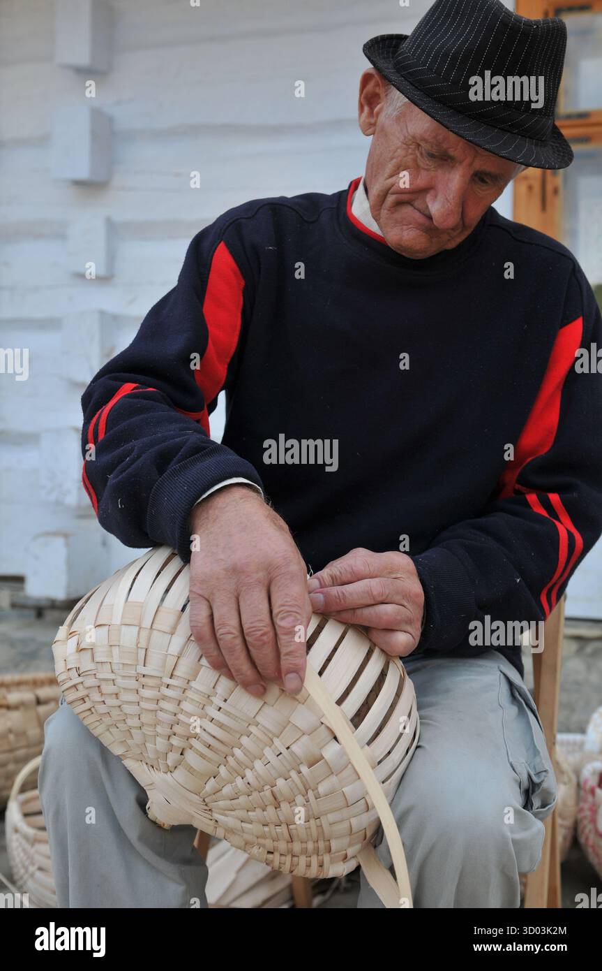 Ein älterer Handwerker, der im Museum für Volksarchitektur in Sanok, Polen, einen Strohkorb von Hand webt. Schlüsselwörter (42): Stockfoto