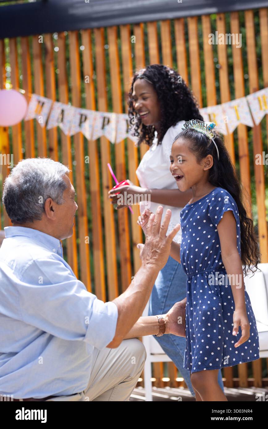 Großvater spielt mit Enkelin, Mutter lächelt auf einer Geburtstagsparty im Freien. Familie, Feier, Glück, draußen, Picknick, Multigenerational || Modell veröffentlicht Stockfoto