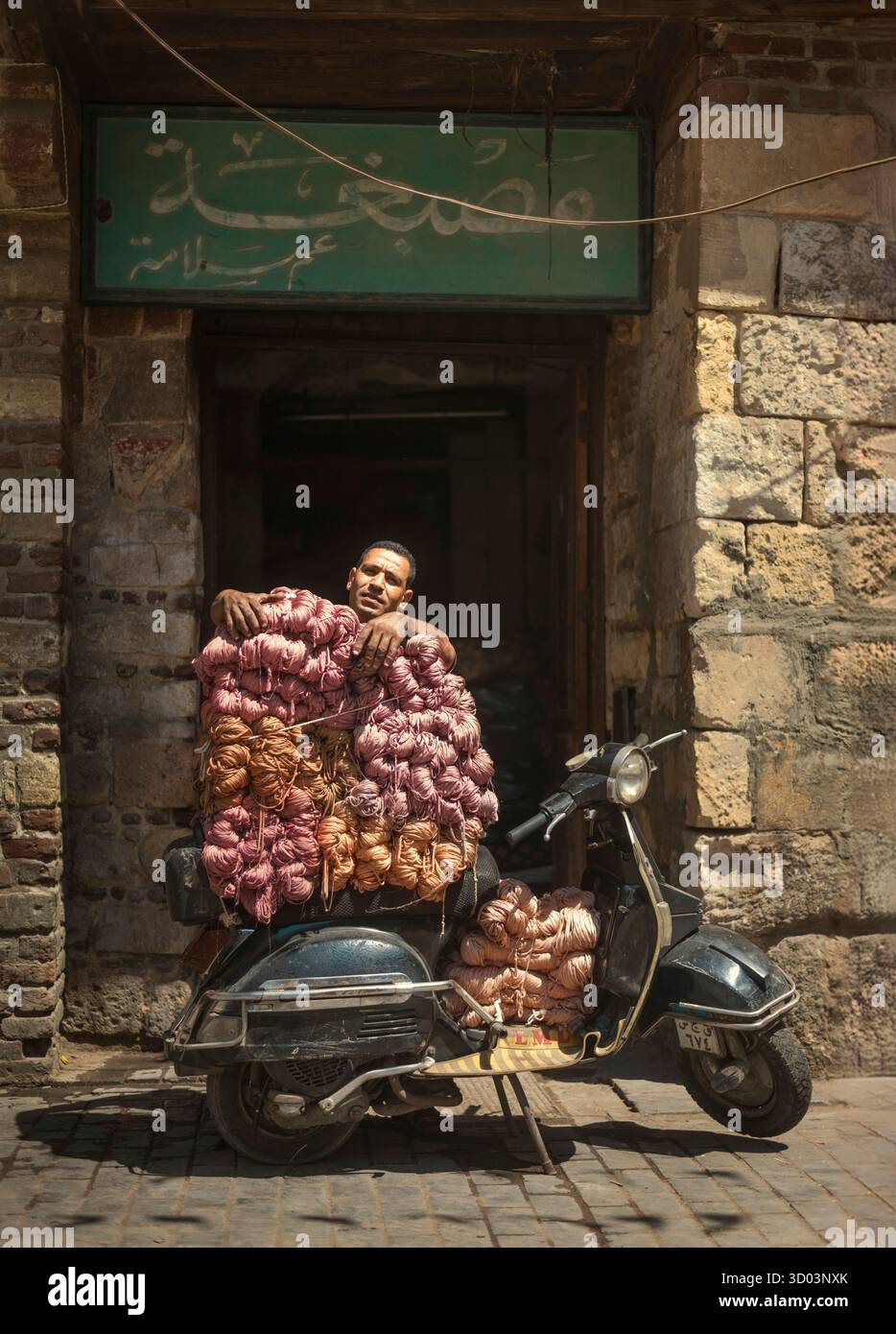 Ein Mann, der vor einer Garnfärberei wartet, mit seinem Vespa-Moped, beladen mit farbigen Garnen, um ihn an Märkte in Old Cairo, Ägypten, zu liefern Stockfoto