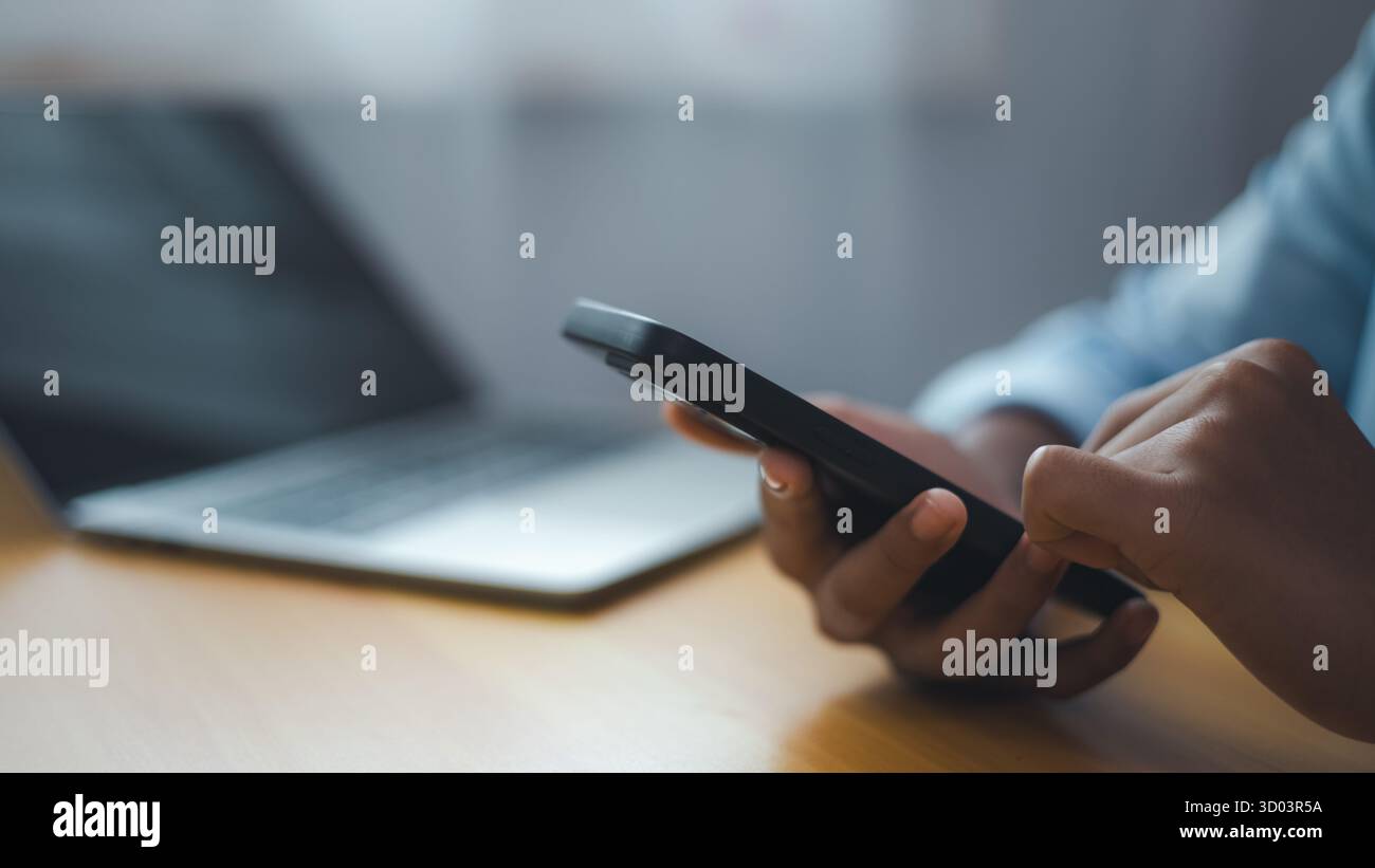 Nahaufnahme einer Geschäftsperson mit Smartphone und Laptop auf dem Schreibtisch. Modernes Kommunikations- und mobiles Arbeitskonzept, das die digitale Verbindung und Stockfoto