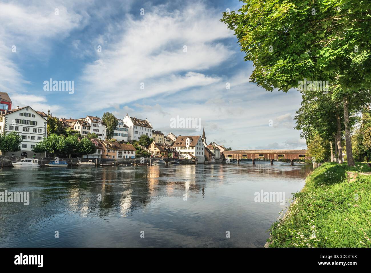 Blick auf die mittelalterliche Altstadt von Diessenhofen und die hölzerne überdachte Brücke über den Hochrhein zwischen der Schweiz und Gailingen, Deutschland. Historische Giebelhäuser und ein Kirchturm säumen das Ufer, mit Booten, die im ruhigen Wasser verankert sind. Stockfoto Blick auf die mittelalterliche Altstadt von Diessenhofen und die hölzerne überdachte Brücke über den Hochrhein zwischen der Schweiz und Gailingen, Deutschland. Historische Giebelhäuser und ein Kirchturm säumen das Ufer, mit Booten, die im ruhigen Wasser verankert sind. Stockfoto