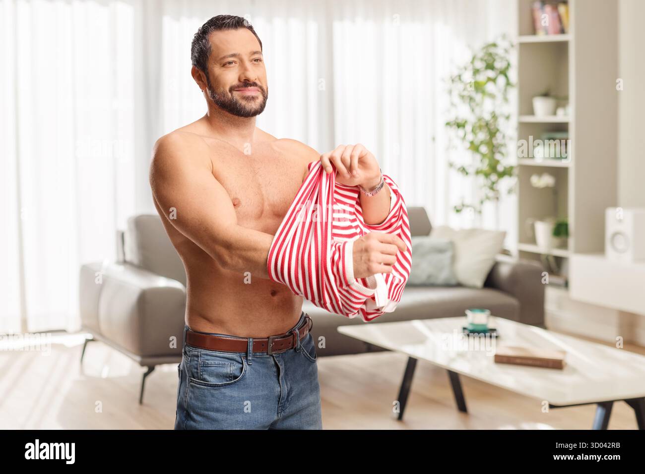 Lächelnder Mann, der ein gestreiftes T-Shirt im Wohnzimmer anzieht Stockfoto