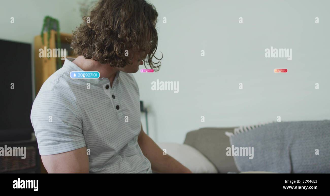 Sitzender Mann mittleren Alters mit henley-Hemd auf grauem Sofa im Wohnzimmer, mit Fernseher, Pflanze Stockfoto