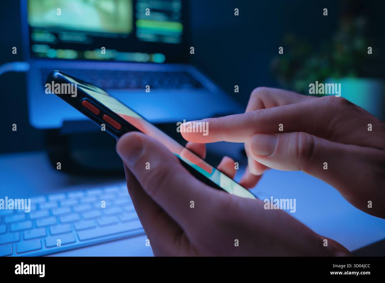Nahaufnahme von Personen, die nachts mit Social-Media-Feed auf dem Smartphone-Bildschirm mit Laptop im Hintergrund aufzeichnen. Digitale sucht und moderne Online-Gewohnheiten. Stockfoto