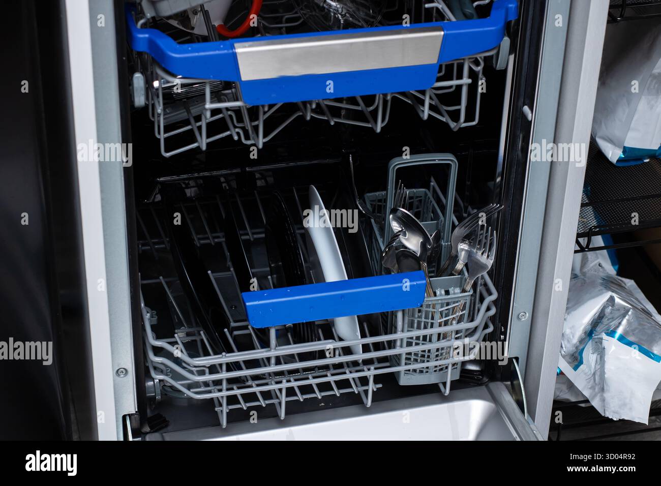 Ein moderner Geschirrspüler mit organisierter Inneneinrichtung mit sauberen Tellern, Utensilien und Kochgeschirr, bereit für den Gebrauch. Effiziente Reinigung für eine geschäftige Küche. Stockfoto