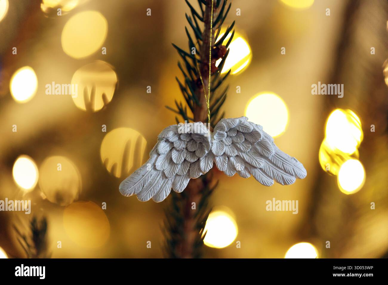 Nahaufnahme eines weißen Engelsflügels, der an einem Weihnachtsbaum hängt, mit warmen Bokeh-Lichtern im Hintergrund Stockfoto