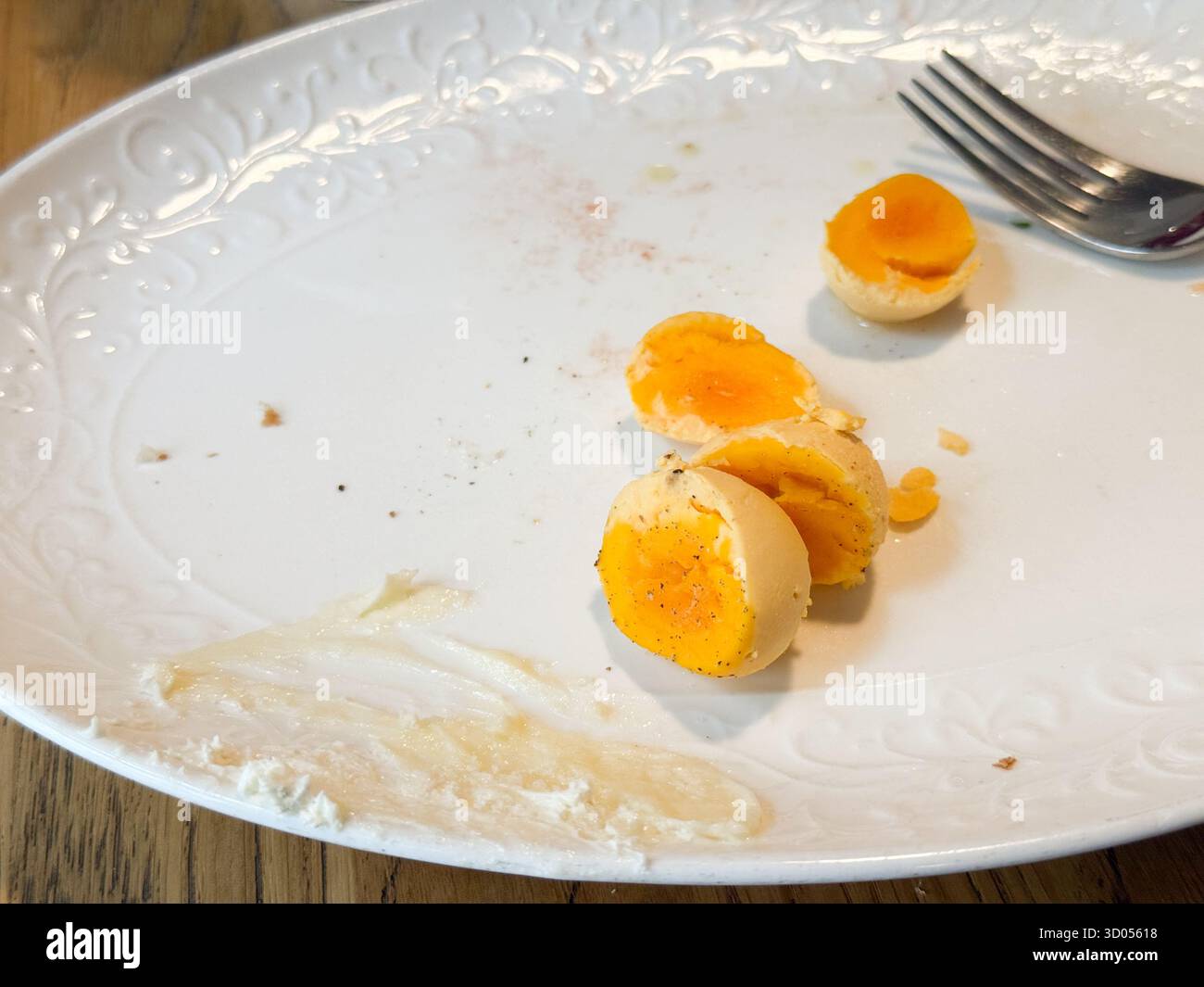 Leerer Frühstücksteller mit übrig gebliebenen gekochten Eiern und Gabel. Minimalismus, Routine und alltägliche Einfachheit im Café-Dining-Moment Stockfoto