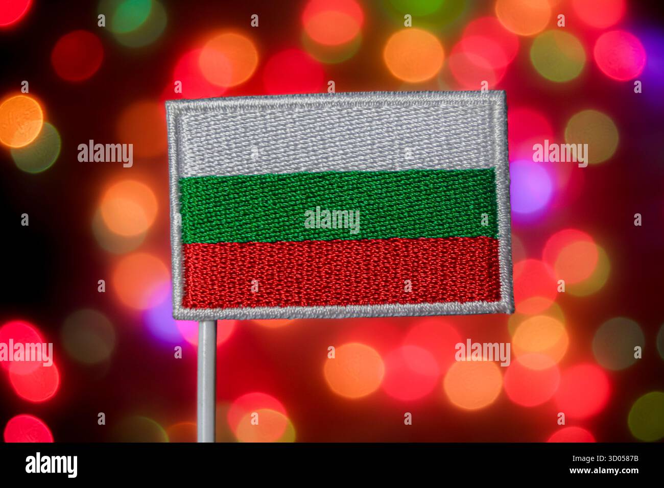 Bulgarische Nationalflagge gegen bunte Bokeh-Lichter. Europäisch-slawische Kultur, Nationalstolz, Unabhängigkeitstag und Weihnachtsmedien. Stockfoto