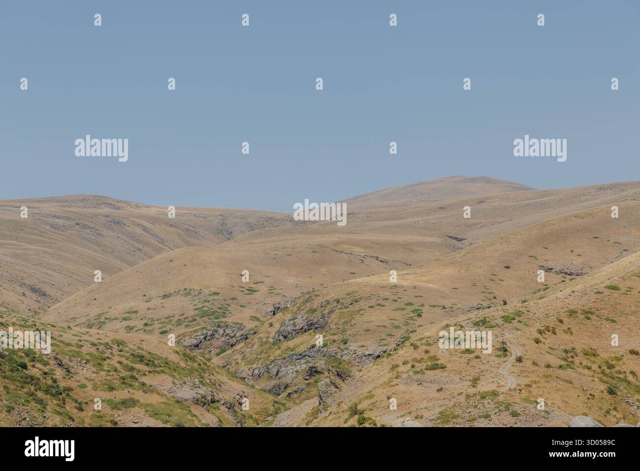 Blick auf hügelige, trockene Hügel, die in das warme Licht der Sonne getaucht sind und eine ruhige Landschaft unter einem klaren blauen Himmel schaffen, Lake Kari, Shirak Provinz, Arm Stockfoto