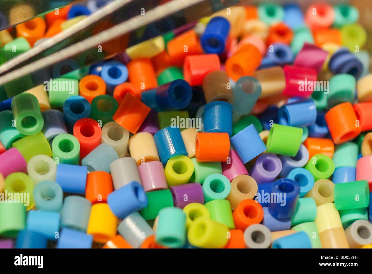 Farbenfrohe Perler-Perlen mit Pinzette. Unterhaltsame Hintergrundinformationen für DIY-Blogs, Lernmaterialien für Kinder, Feinmotorik oder abstrakte Daten. Stockfoto