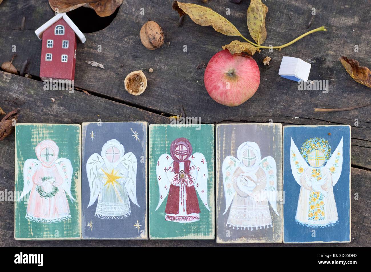 Rustikale Ferienanlage mit Holzengelblöcken, Miniaturhaus, Apfel, Nüsse und Herbstlaub auf verwitterter Holzoberfläche. Stockfoto
