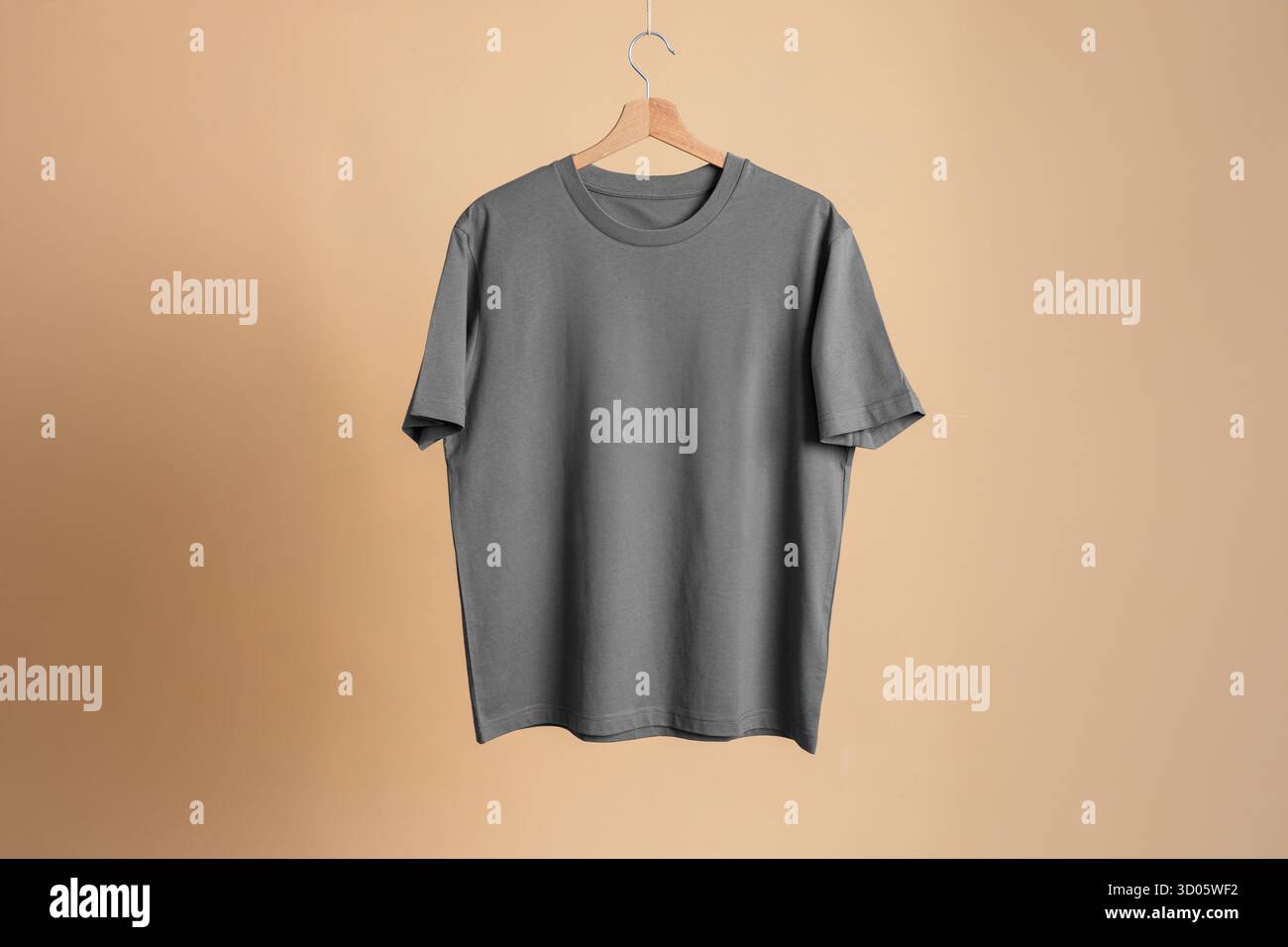 Dunkelgraues T-Shirt-Modell auf hölzernem Aufhänger, beigefarbener Hintergrund. Anpassbare E-Commerce-Vorlage. Hochwertige Baumwolle. Vielseitige neutrale Farben für individuelle Individualisierung Stockfoto