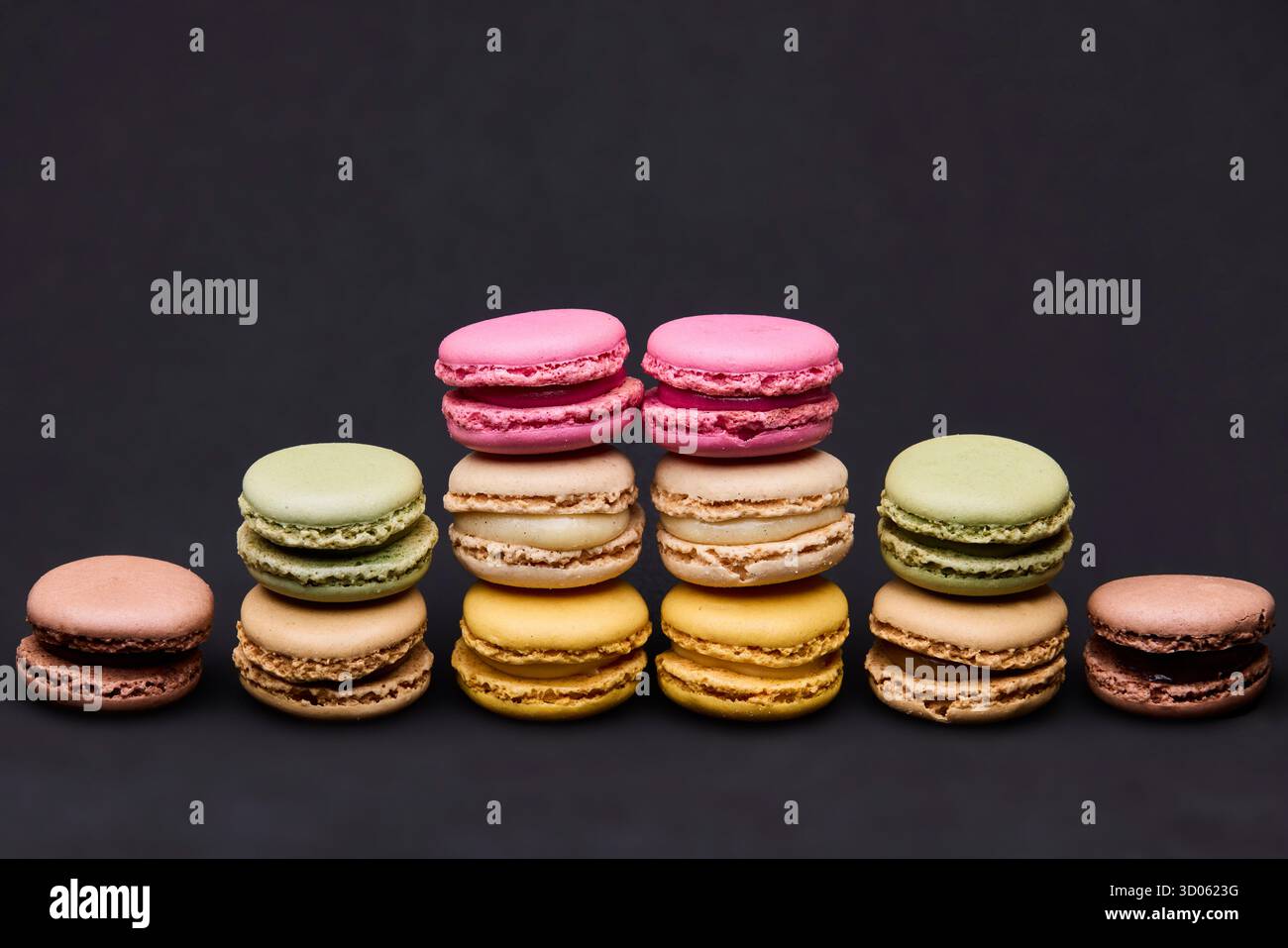 Verschiedene bunte Macarons in Reihen auf dunklem Hintergrund. Das symmetrische Layout sorgt für einen modernen, sauberen Stil, der für Food Branding und Packagi geeignet ist Stockfoto