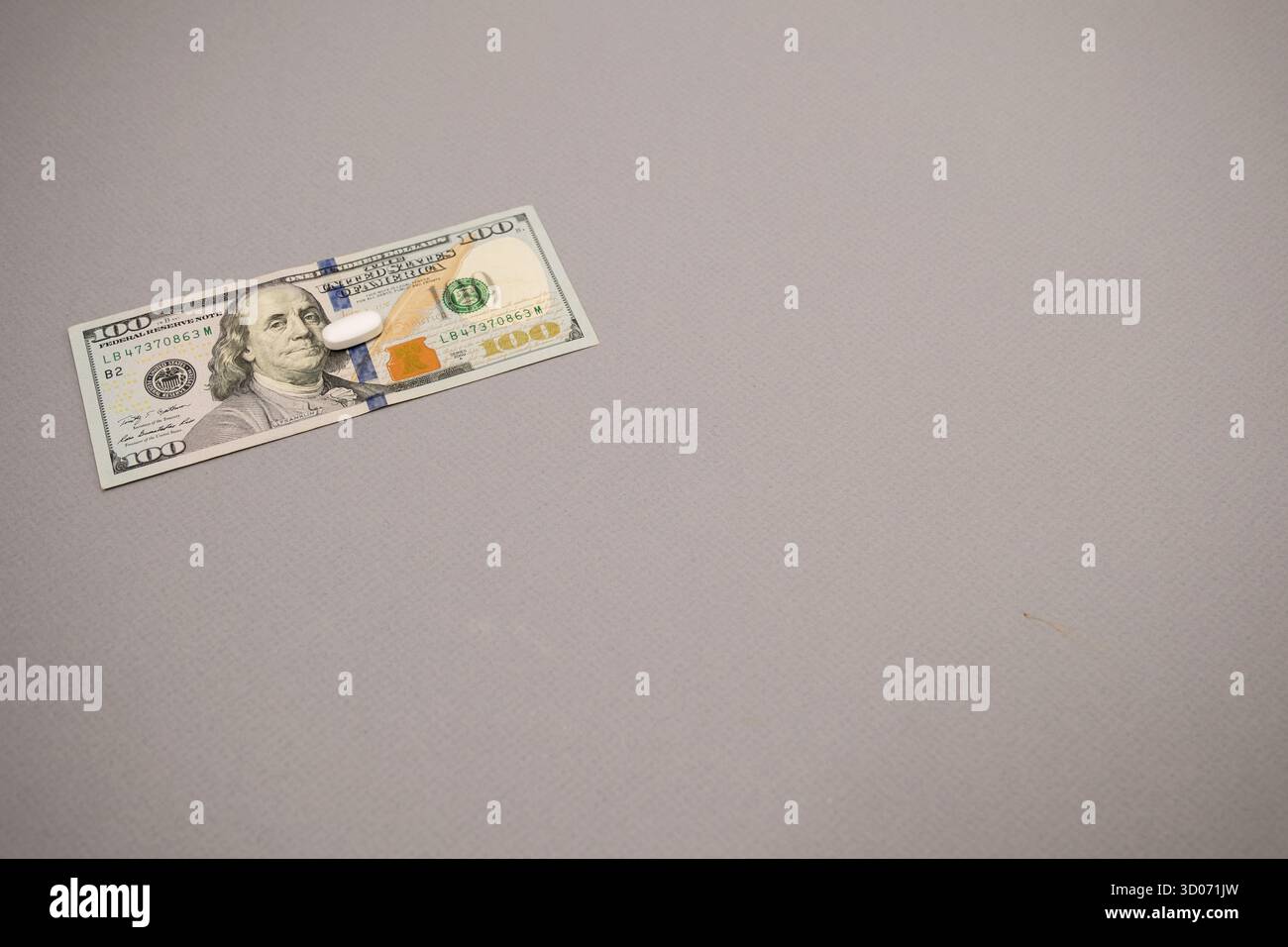 Eine einzige weiße Rezeptpille liegt auf einem 100-Dollar-Schein mit grauem Schwarzgrund. Stockfoto