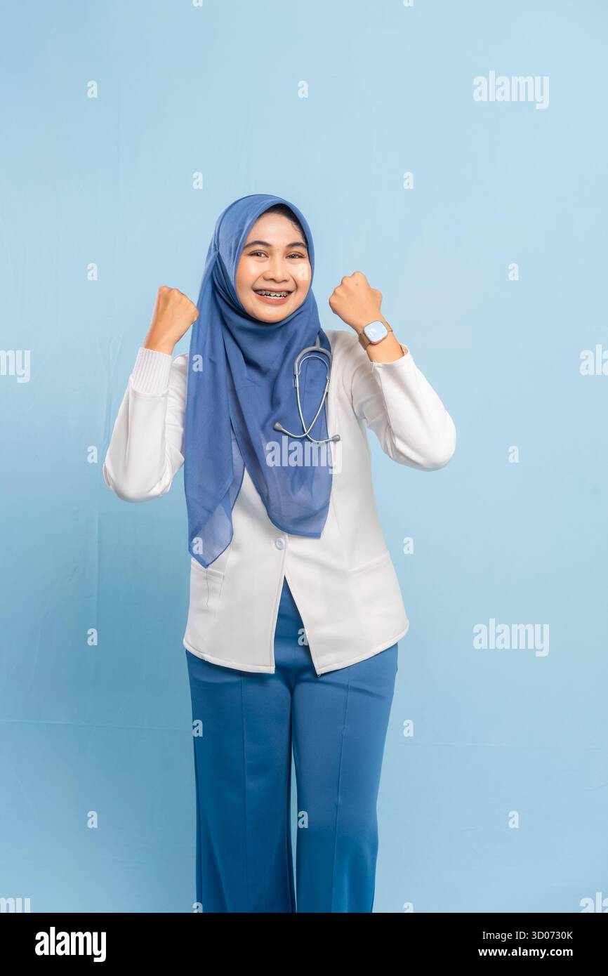 Porträt eines selbstbewussten asiatischen muslimischen Arztes oder Krankenschwestern, der Stärke oder Entschlossenheit zeigt und vor blauem Hintergrund lächelt. Stockfoto