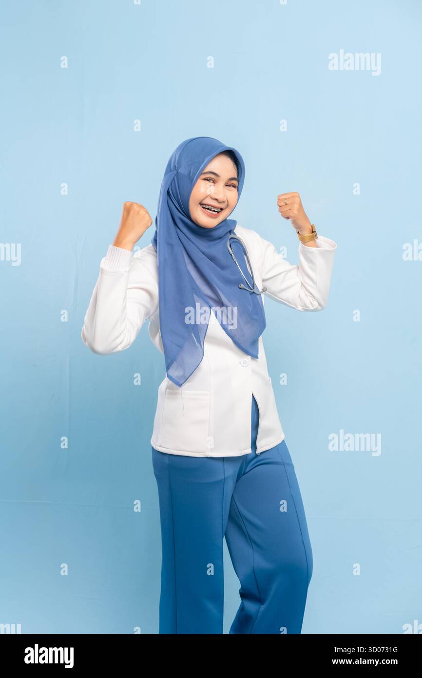 Porträt eines selbstbewussten asiatischen muslimischen Arztes oder Krankenschwestern, der Stärke oder Entschlossenheit zeigt und vor blauem Hintergrund lächelt. Stockfoto