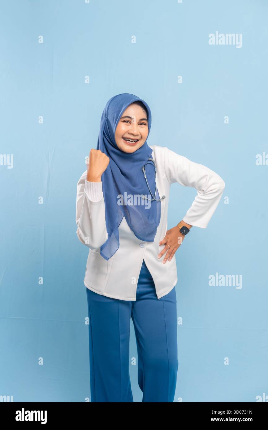 Porträt eines selbstbewussten asiatischen muslimischen Arztes oder Krankenschwestern, der Stärke oder Entschlossenheit zeigt und vor blauem Hintergrund lächelt. Stockfoto