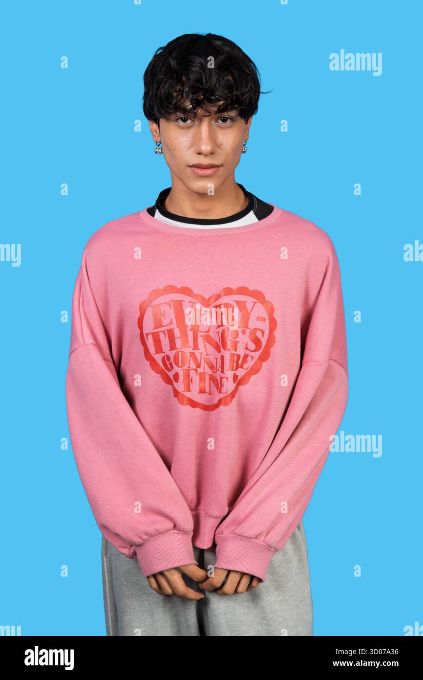 Junge Person posiert in einem Studio, trägt ein rosafarbenes Sweatshirt mit einer positiven Nachricht Stockfoto