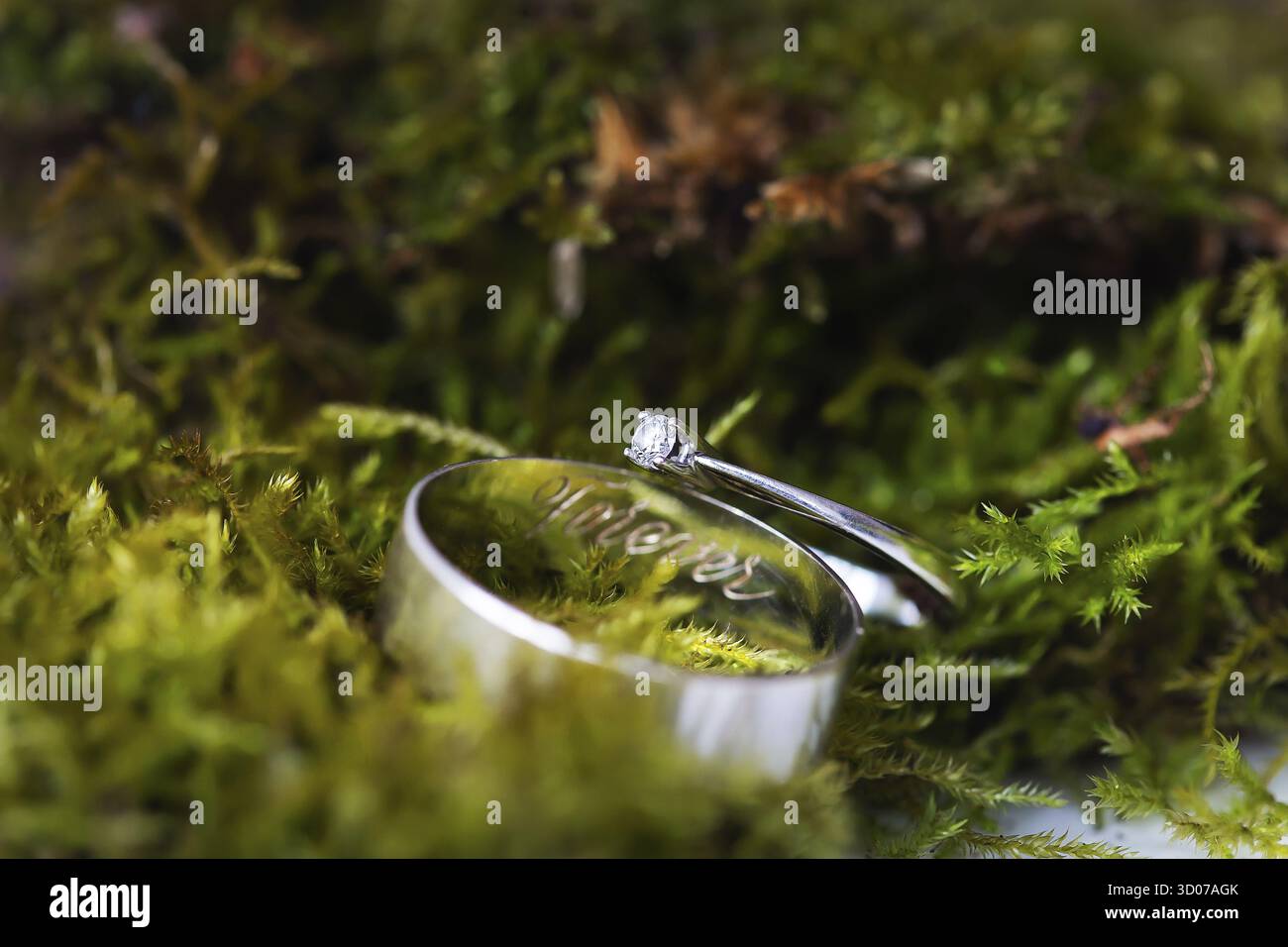 Eleganter Diamantring und Verlobungsring mit Forever Inschrift auf grünem Moos. Schöne Lichter und Sonnenlicht, weicher und selektiver Fokus. Ehe Stockfoto