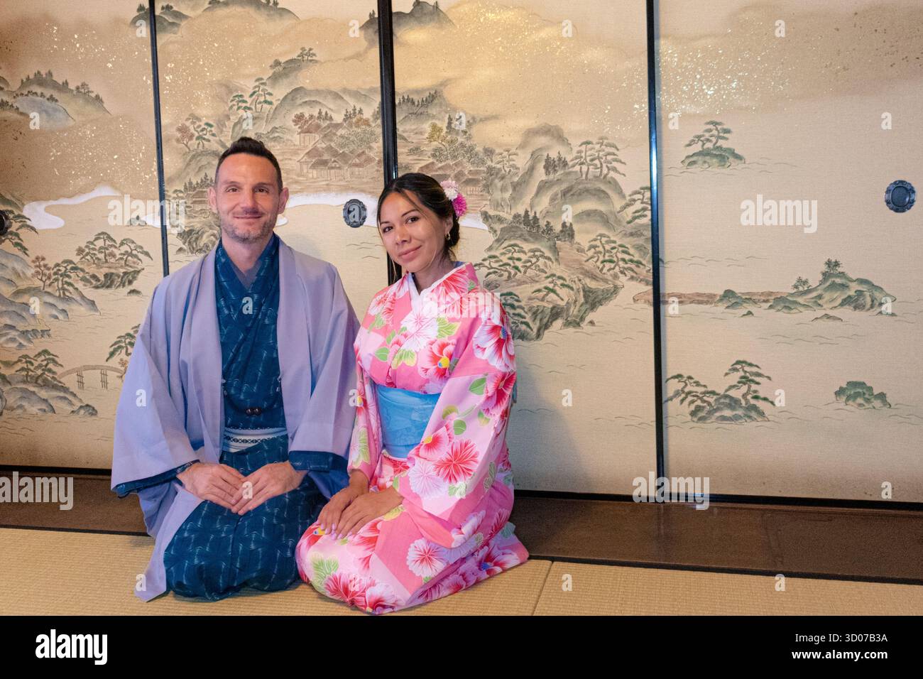 Warmes Bild eines weißen Mannes und einer Latina-Frau, gekleidet als Samurai und Geisha, die zusammen auf einer neutralen Plattform sitzen. Schlägt Verbindungsreisen und authen vor Stockfoto