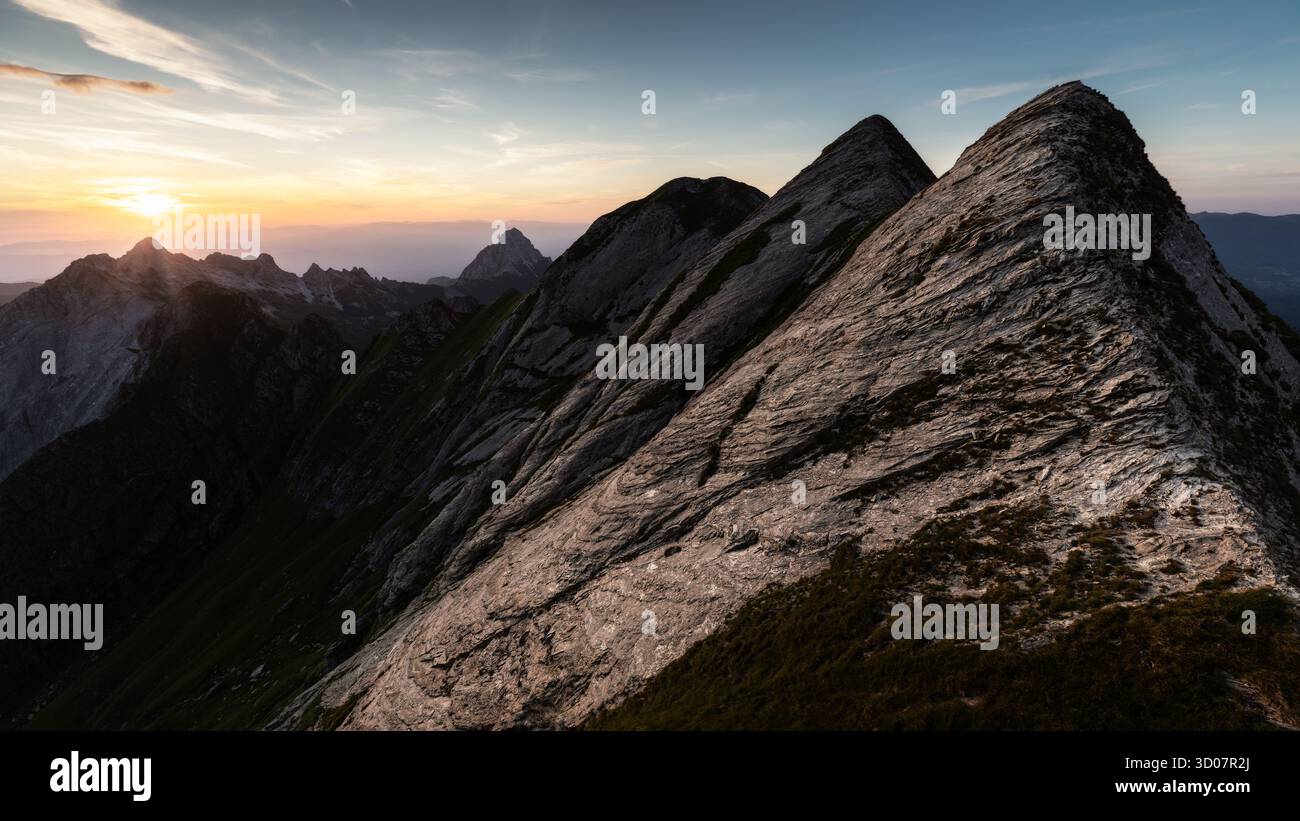 Der Blick auf zerklüftete, sonnenverwöhnte Berggipfel reicht bis in das verblassende Licht unter einem pastellfarbenen Himmel und erzeugt einen dramatischen Kontrast von Licht und Schatten, Carrara, T Stockfoto