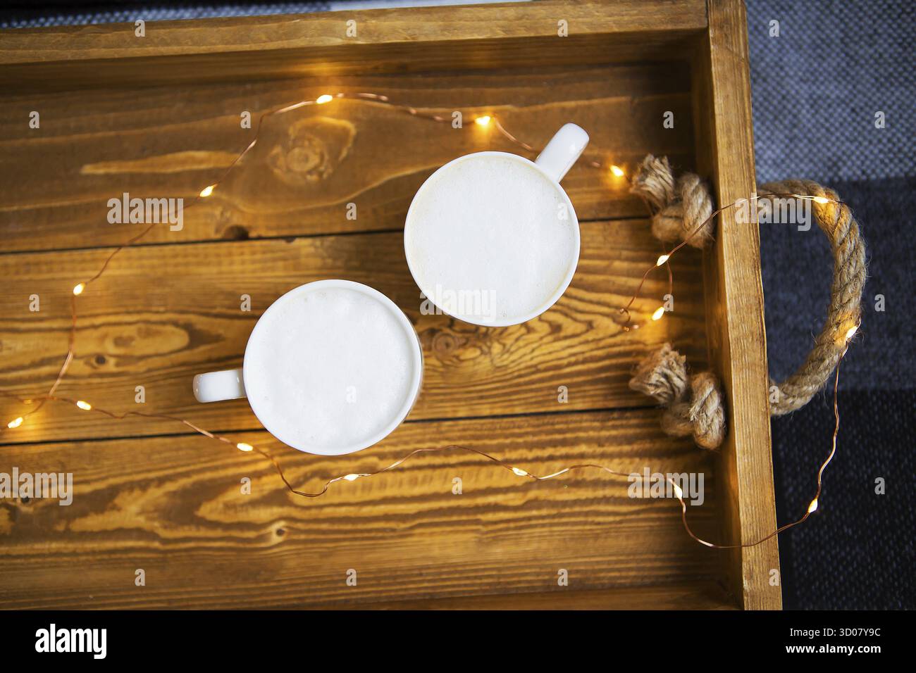 Zwei Tassen Cappuccino stehen auf einem Holztablett mit Lichtern Stockfoto