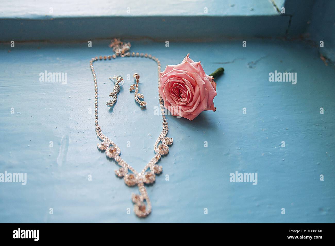 Elegante Rose mit Halskette und Ohrringen auf blauem Hintergrund Stockfoto