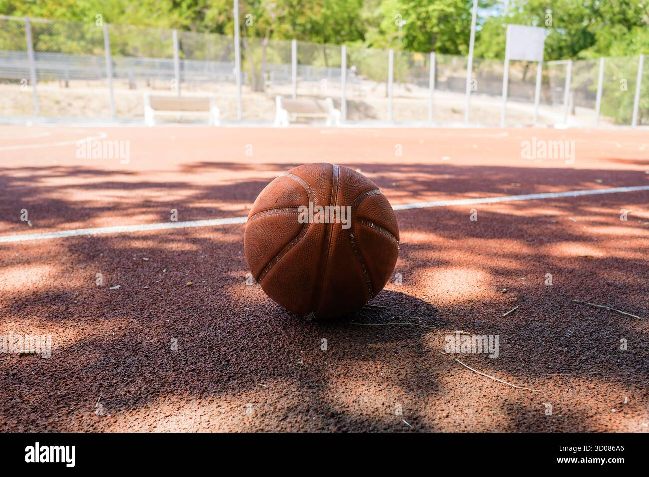 Ein Basketball, der sich an einem klaren, sonnigen Tag auf einem Sportplatz im Freien bei hellem Sonnenlicht ausruhen lässt und perfekt zum Spielen oder Üben geeignet ist Stockfoto