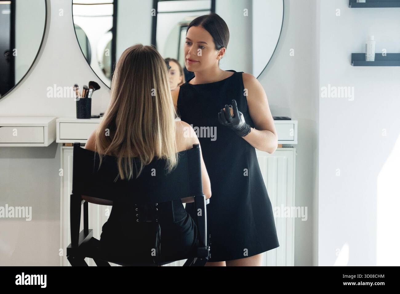 Ein Schönheitsexperte schminkt geschickt einen Kunden, der in einem stilvollen Salon sitzt. Die Atmosphäre ist einladend mit hellem Licht und elegantem Pelz Stockfoto