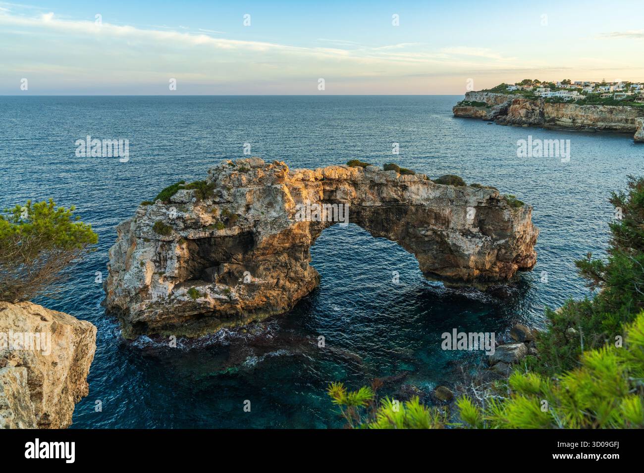 Natursteinbogen im Meer bei Cala Santanyi, Mallorca, glühend im goldenen Sonnenuntergang. Friedliche mediterrane Küstenszene mit dramatischem Rock-Format Stockfoto