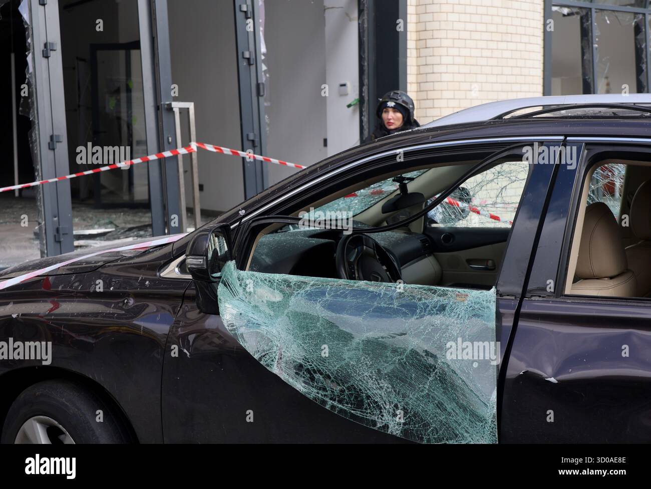 Nicht exklusiv: Ein Polizist in einem Kampfhelm steht hinter einem beschädigten Auto vor einem privaten Kindergarten im Bezirk Kholodnohirskyi, der von t getroffen wurde Stockfoto