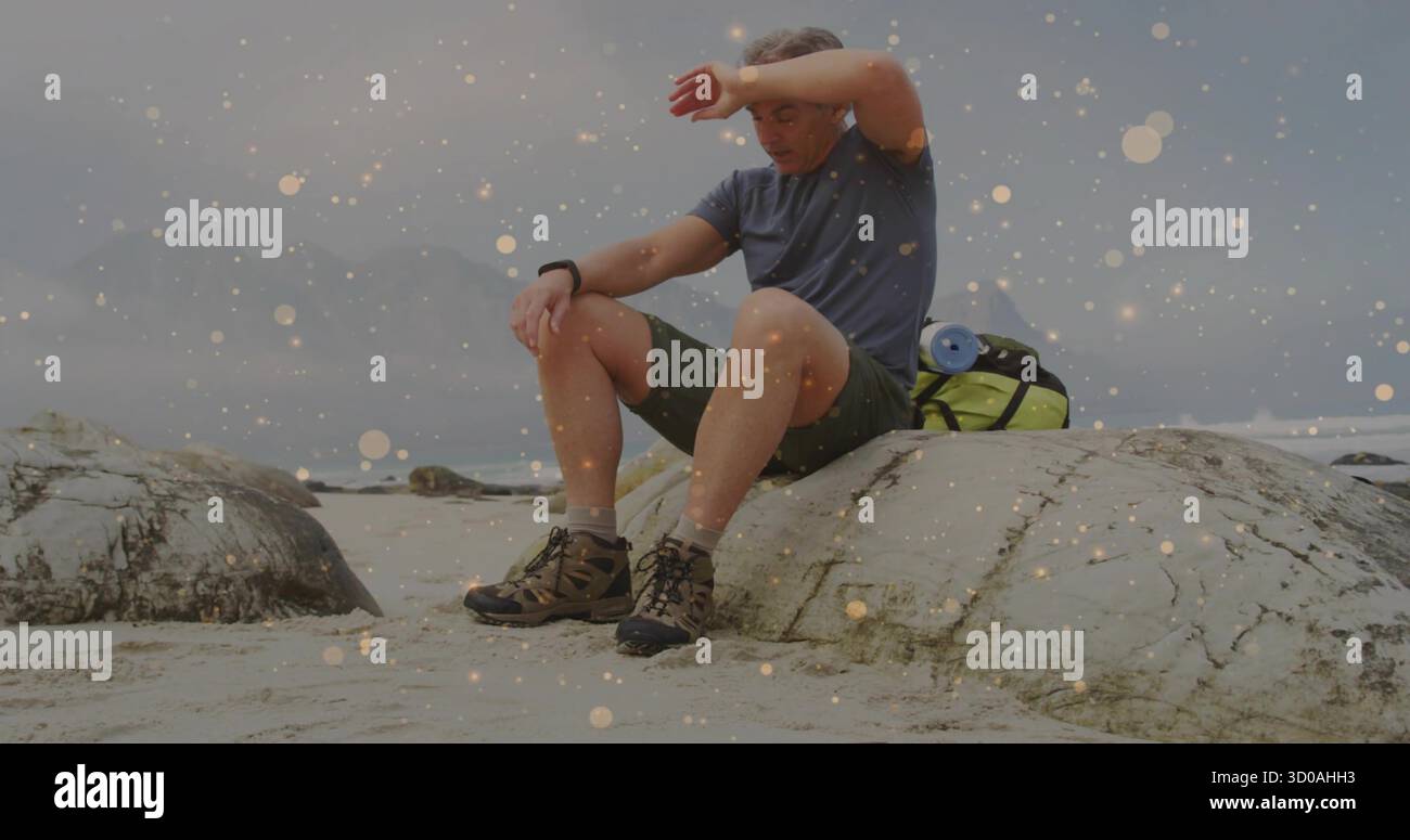 Ruhesuchsänger in Shorts, die den Schweiß von den Brauen auf dem Felsen am Sandstrand abwischen, mit grünem Rucksack Stockfoto