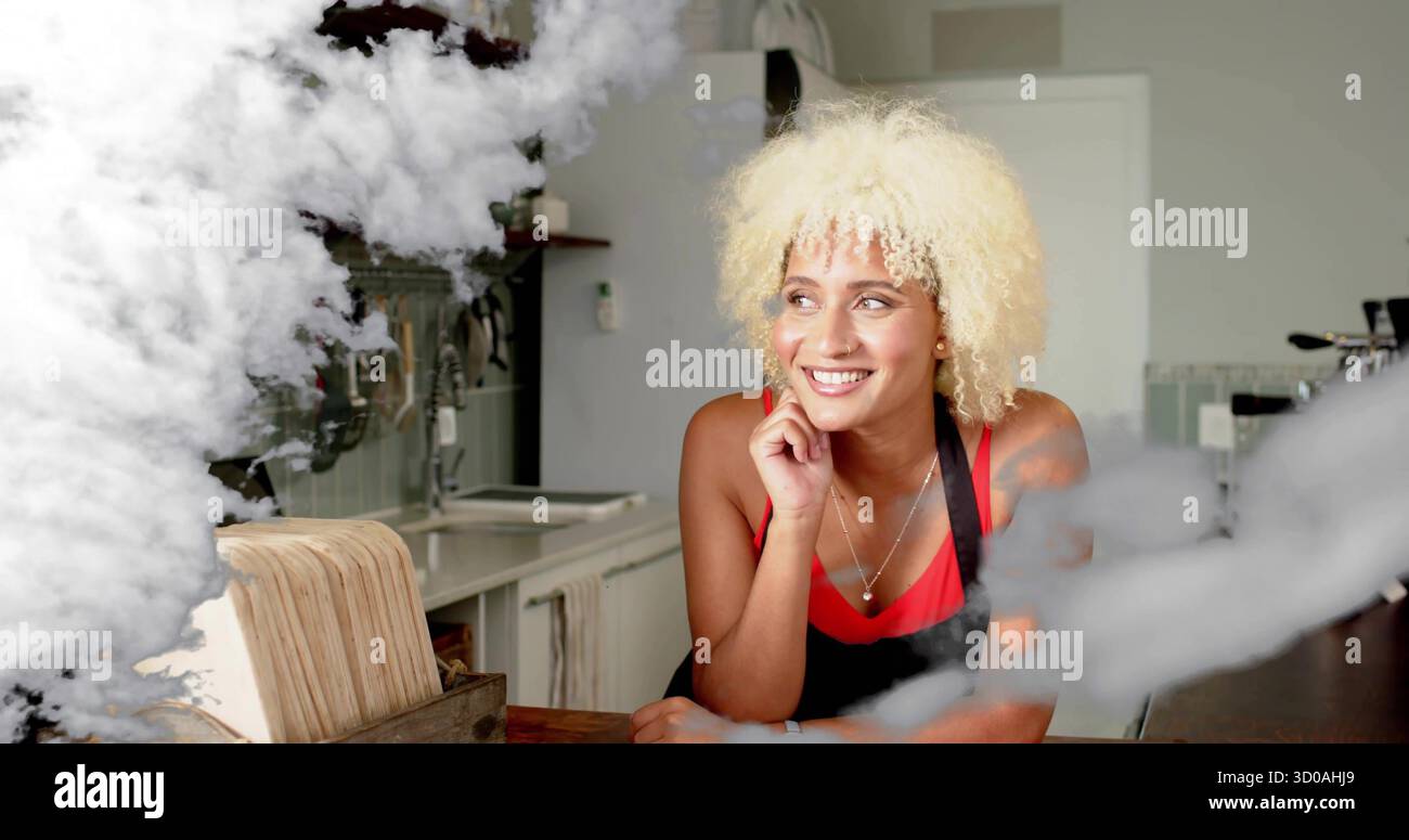 Lehnender Cafe-Arbeiter, der das Kinn auf der Hand liegend in der Café-Küche lächelte, mit Holztheke und Dampf Stockfoto