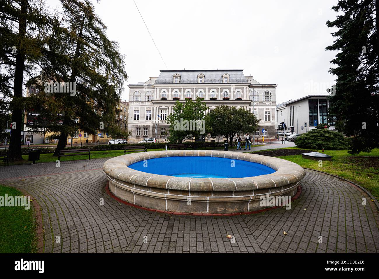 Tarnow, Polen - 10. Oktober 2025: Runder Steinbrunnen mit blauem Becken in einem Park in der Nähe eines historischen Gebäudes in Tarnow, Polen. Stockfoto