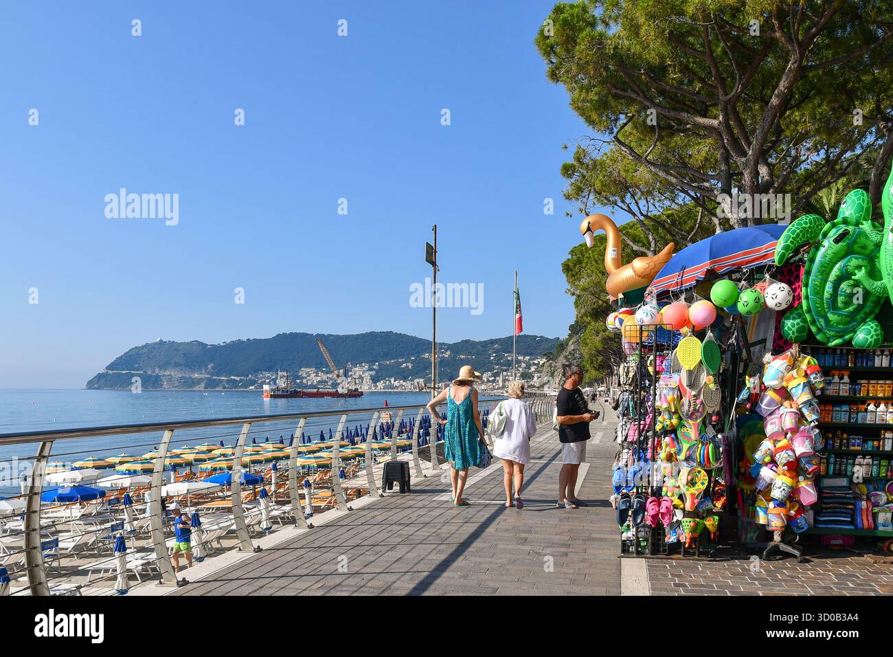 Blick auf die Passeggiata Angelo Ciccione Küste mit einem Souvenirstand, der Strandartikel verkauft, und Capo Mele Landzunge, Alassio (Savona), Ligurien, Italien Stockfoto