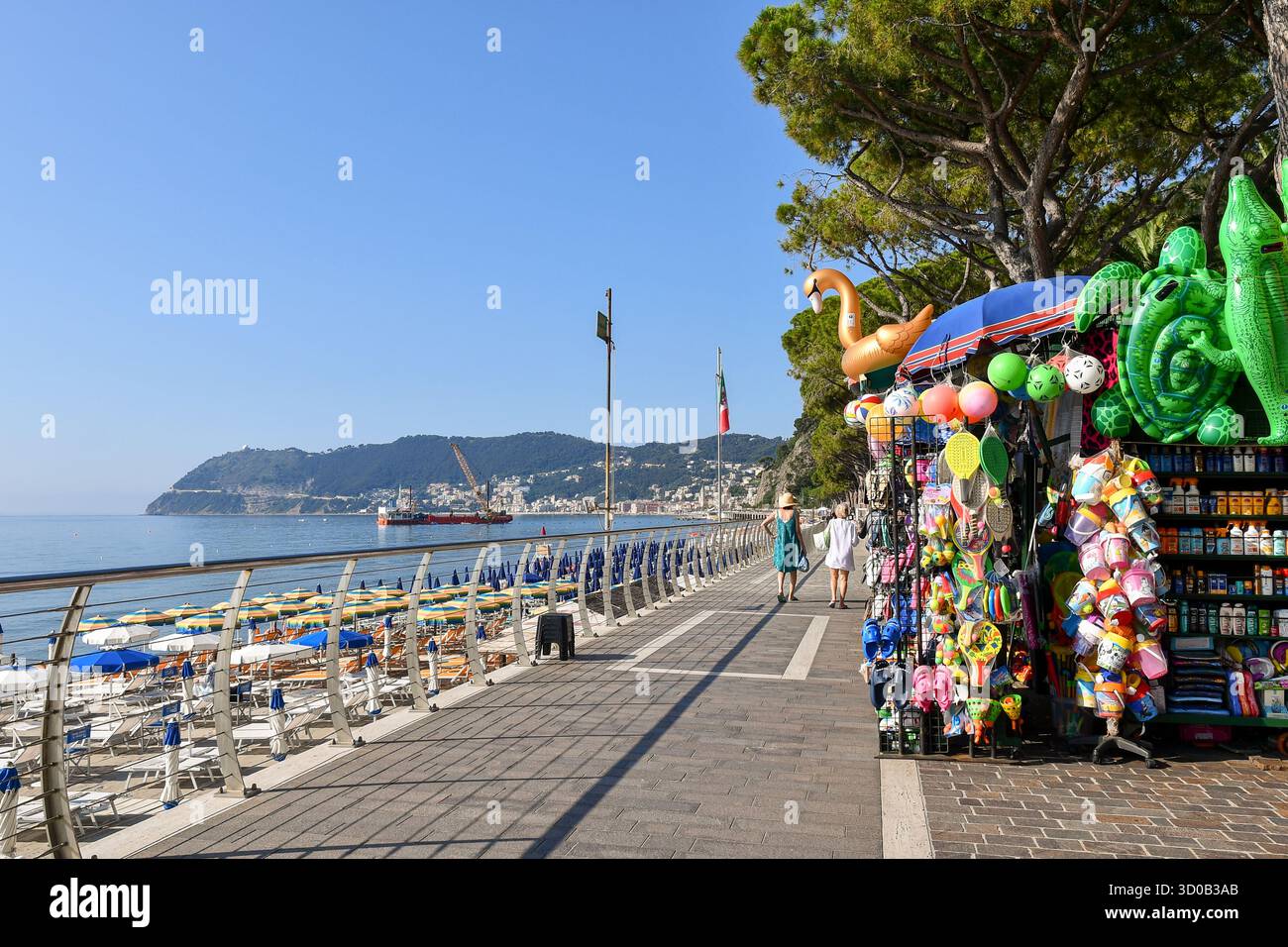 Blick auf die Passeggiata Angelo Ciccione Küste mit einem Souvenirstand, der Strandartikel verkauft, und Capo Mele Landzunge, Alassio (Savona), Ligurien, Italien Stockfoto