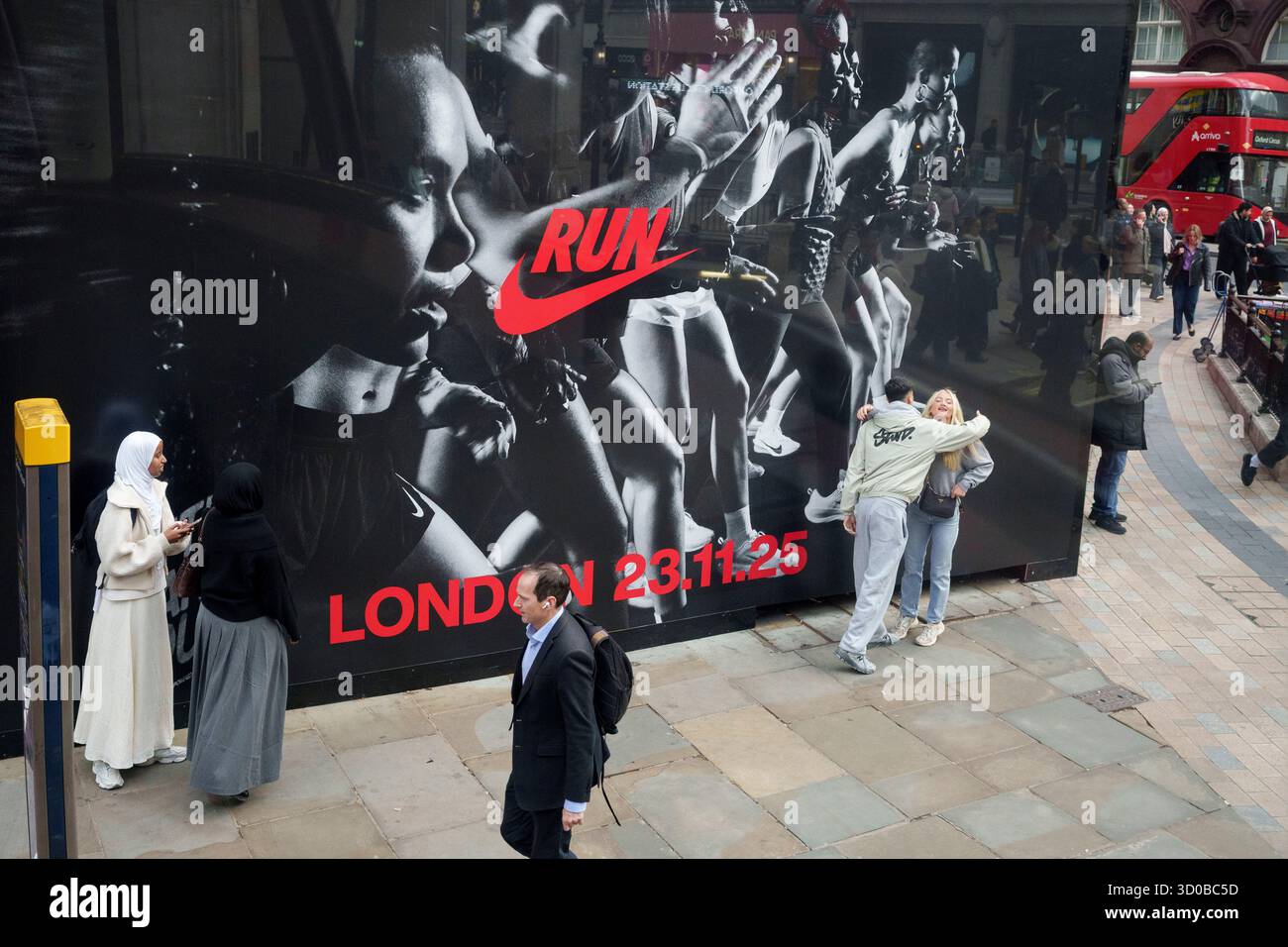 Am 22. Oktober 2025 im Oxford Circus in London, England, laufen die Käufer unter einer Werbetafel für die Nike Sportmarke. Das Datum des 23. November 2025 bezieht sich auf ein Event, das Nike an diesem Tag auf der Excel ausrichtet, bei dem Sportlerinnen mit einer 1K-Qualifikation konfrontiert werden, die festlegt, in welchem von drei 10K-Rennen sie antreten können, sowie auf einer geeigneten Strecke, die für Geschwindigkeit und Ausdauer ausgelegt ist. Stockfoto