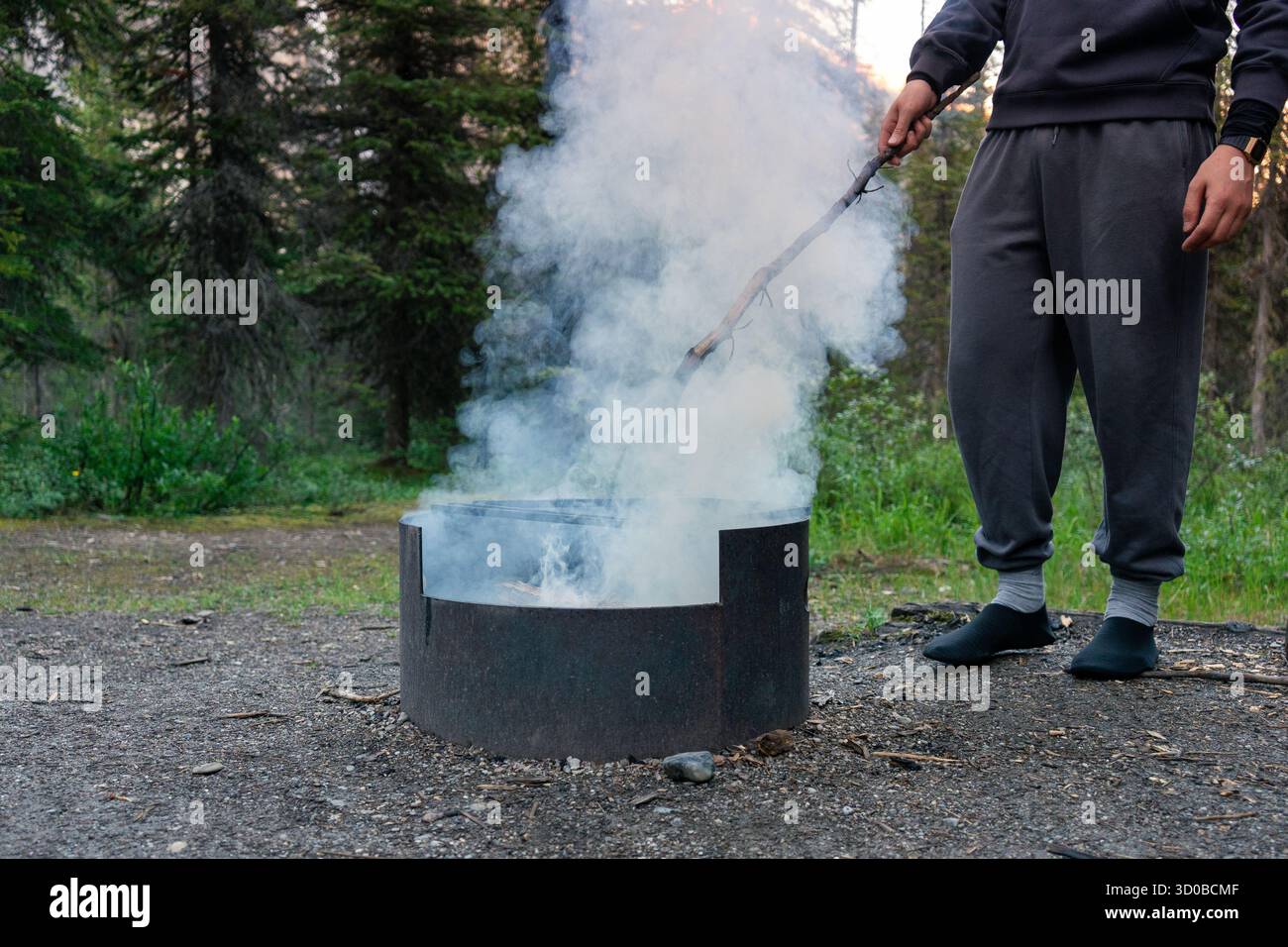 Person, die ein Rauchfeuer in einem Metallfeuer in einem Waldgebiet pflegt. Takakkaw Falls, BC Stockfoto