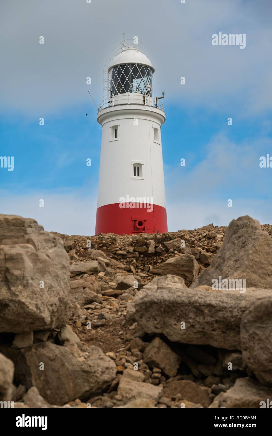 Ein rot-weißer Leuchtturm steht auf einem Felsvorsprung vor einem blauen Himmel. Stockfoto