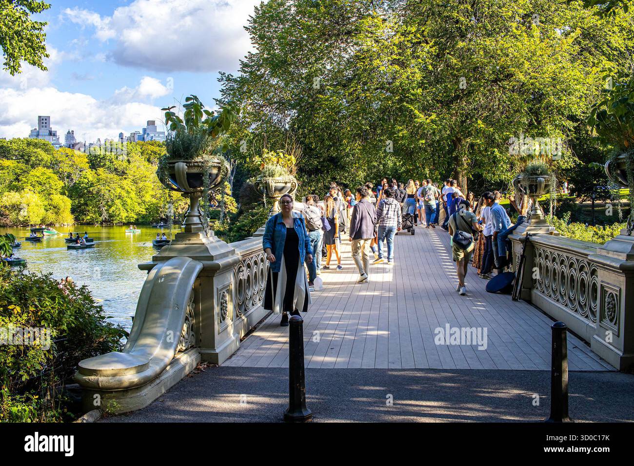 Menschen, die an einem sonnigen Sommertag auf der Bow Bridge über den See im Central Park spazieren gehen. Touristen genießen den öffentlichen Park in Manhattan, New York City. Stockfoto