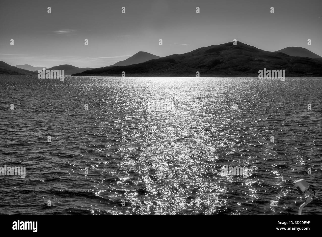 Sonnenlicht reflektiert auf dem Meer mit fernen Hügeln auf den schottischen Inseln in Schwarz-weiß Stockfoto