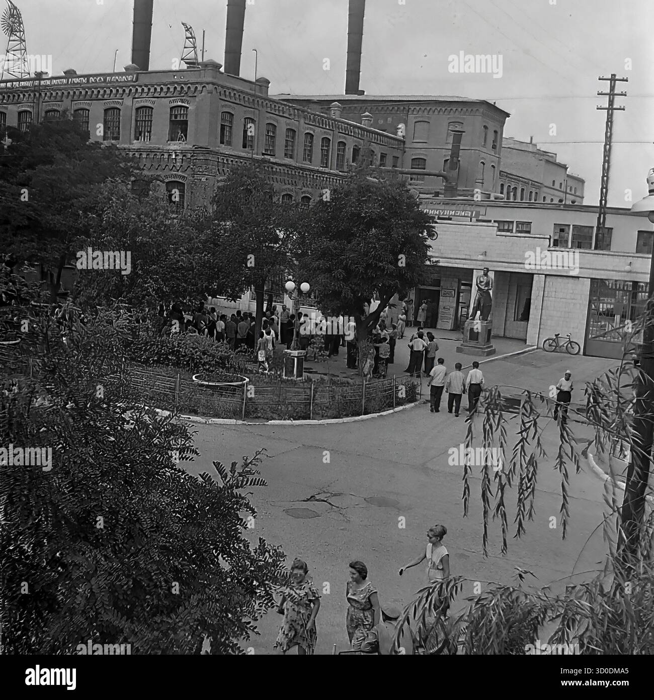 Eine aus der Luft gezogene Hochwinkelansicht des Haupteingangs (prokhodnaya) der Armature-Isolator-Anlage (AIZ) in Sloviansk, 1970er Jahre Dieses Archivfoto aus der UdSSR, der ukrainischen SSR, zeigt eine große Menge von Arbeitern, die sich auf dem Fabrikplatz zu einer Feier versammelt haben (Ballons sind sichtbar). Der Hintergrund wird von den massiven, historischen Backsteingebäuden (Tsekh) mit hohen Schornsteinen dominiert. Dieses Bild fängt die klassische sowjetische Industrielandschaft und die Fabrik als Zentrum des gesellschaftlichen Lebens ein. Ein wertvolles Dokument über das friedliche industrielle Leben im Donbass vor dem Krieg Stockfoto