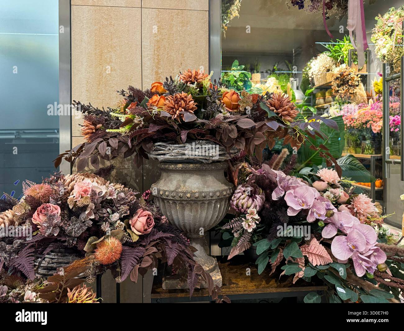 Eine große herbstliche Blume mit Orchideen, Rosen und getrockneter Flora in tiefen, gedämpften Farben überfließt aus einer antiken Urne. Stockfoto