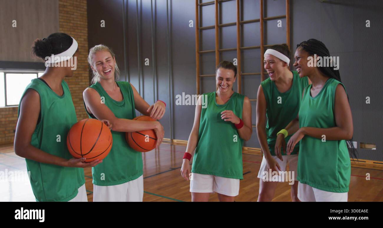 Lachende Basketballkollegen tragen Trikots, stehen im Fitnessstudio, mit Kletterstangen und Basketbälle Stockfoto